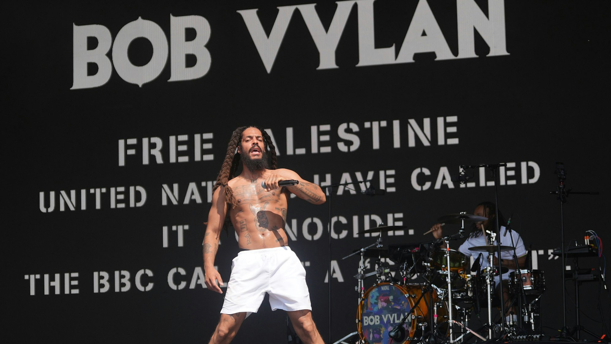 Ein Bob Vylan-Musiker steht beim Auftritt während des Glastonbury Festivals vor dem Schriftzug „Free Palestine – United Nations have call it a genocide“. Zwei Bands haben die Bühne des weltbekannten Festivals für antiisraelische Parolen und Kritik an der britischen Regierung genutzt.