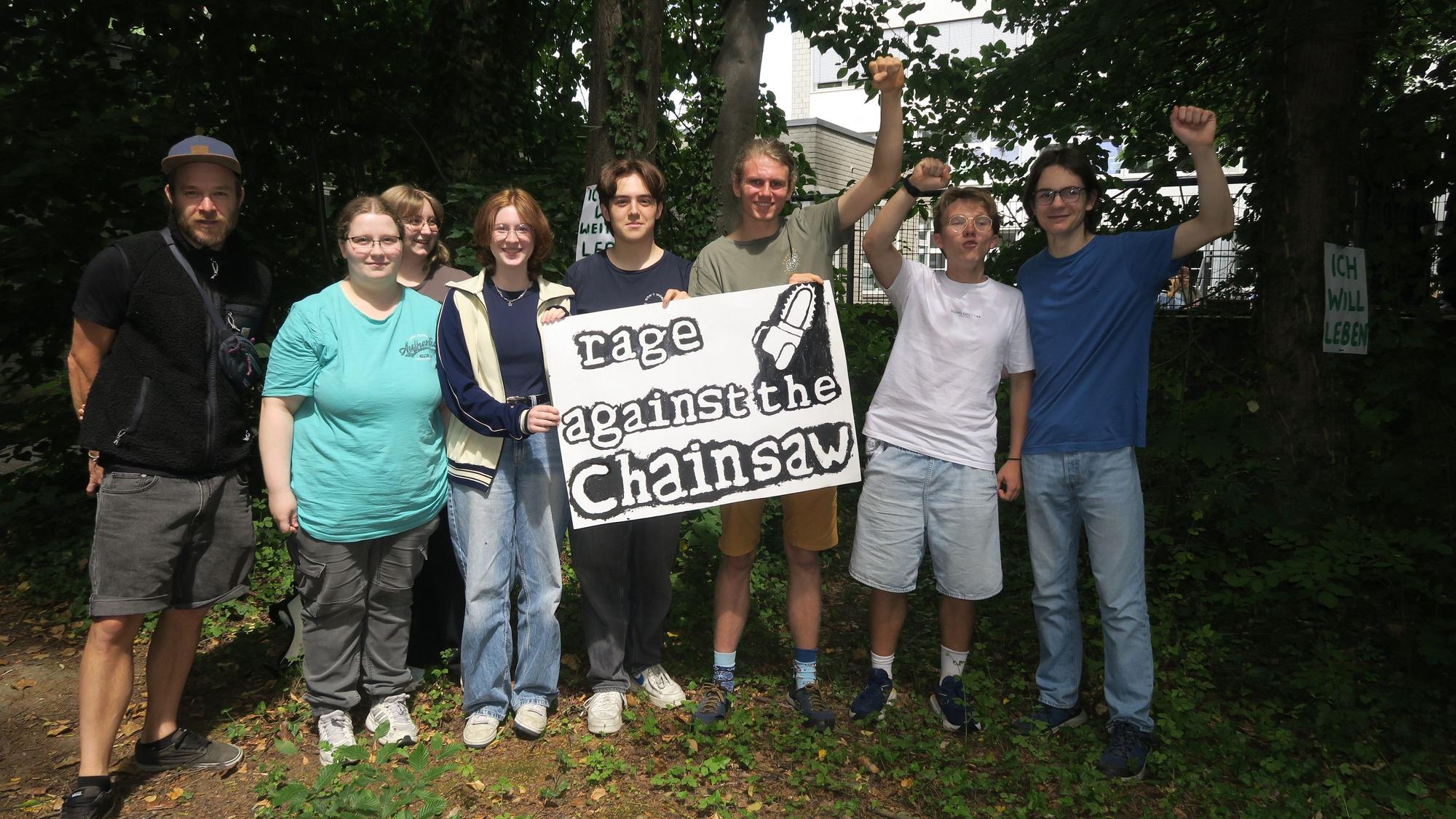 Schüler stehen unter Bäumen, in den Händen haben sie ein Plakat mit der Aufschrift Rage against the chainsaw (Wut gegen die Kettensäge).