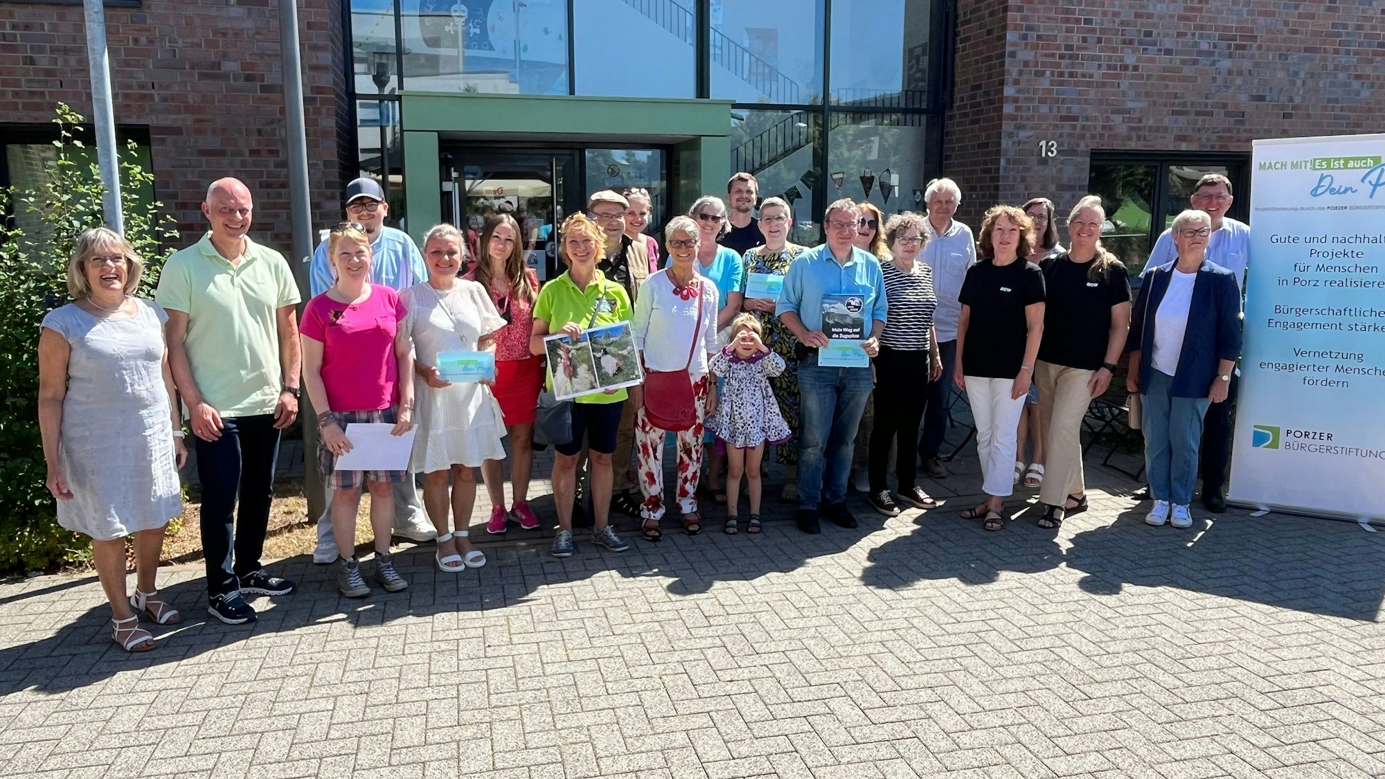 Viele Menschen stehen im Halbkreis vor einem Gebäude mit einer gläsernen Eingangstür.