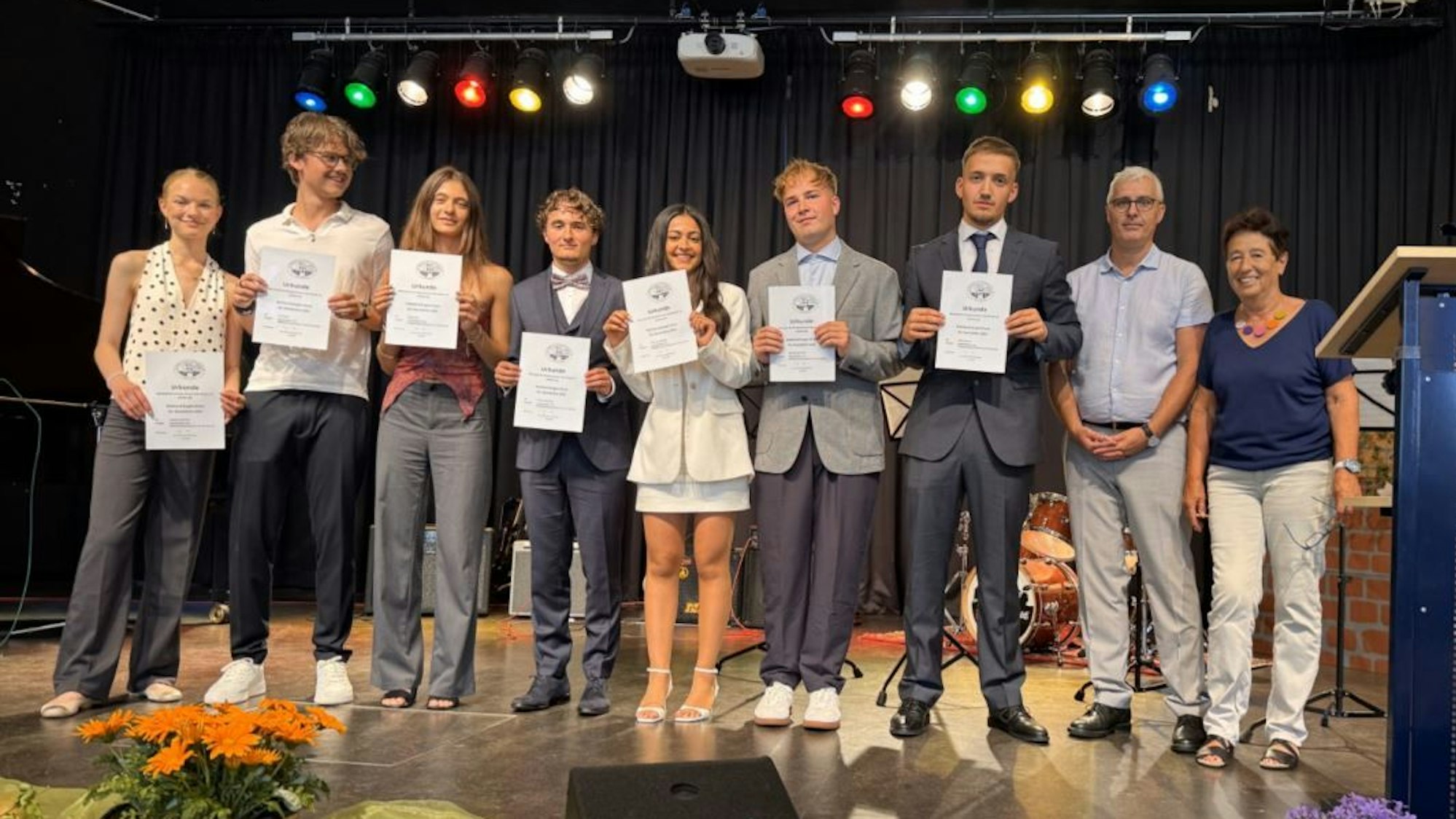 Sieben Schülerinnen und Schüler stehen nebeneinander auf einer Bühne.
