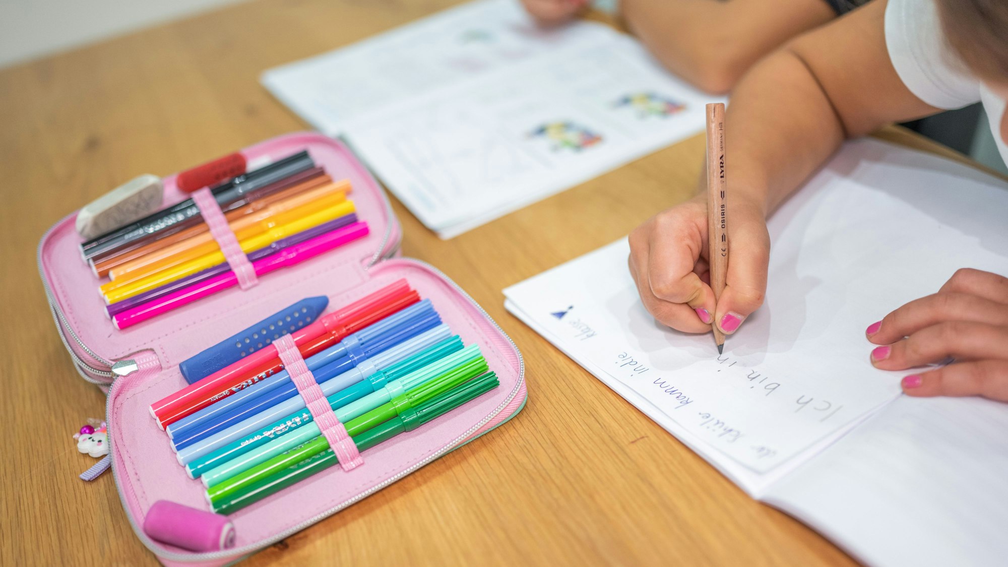 Grundschüler sitzen an einem Tisch und erledigen Schulaufgaben.