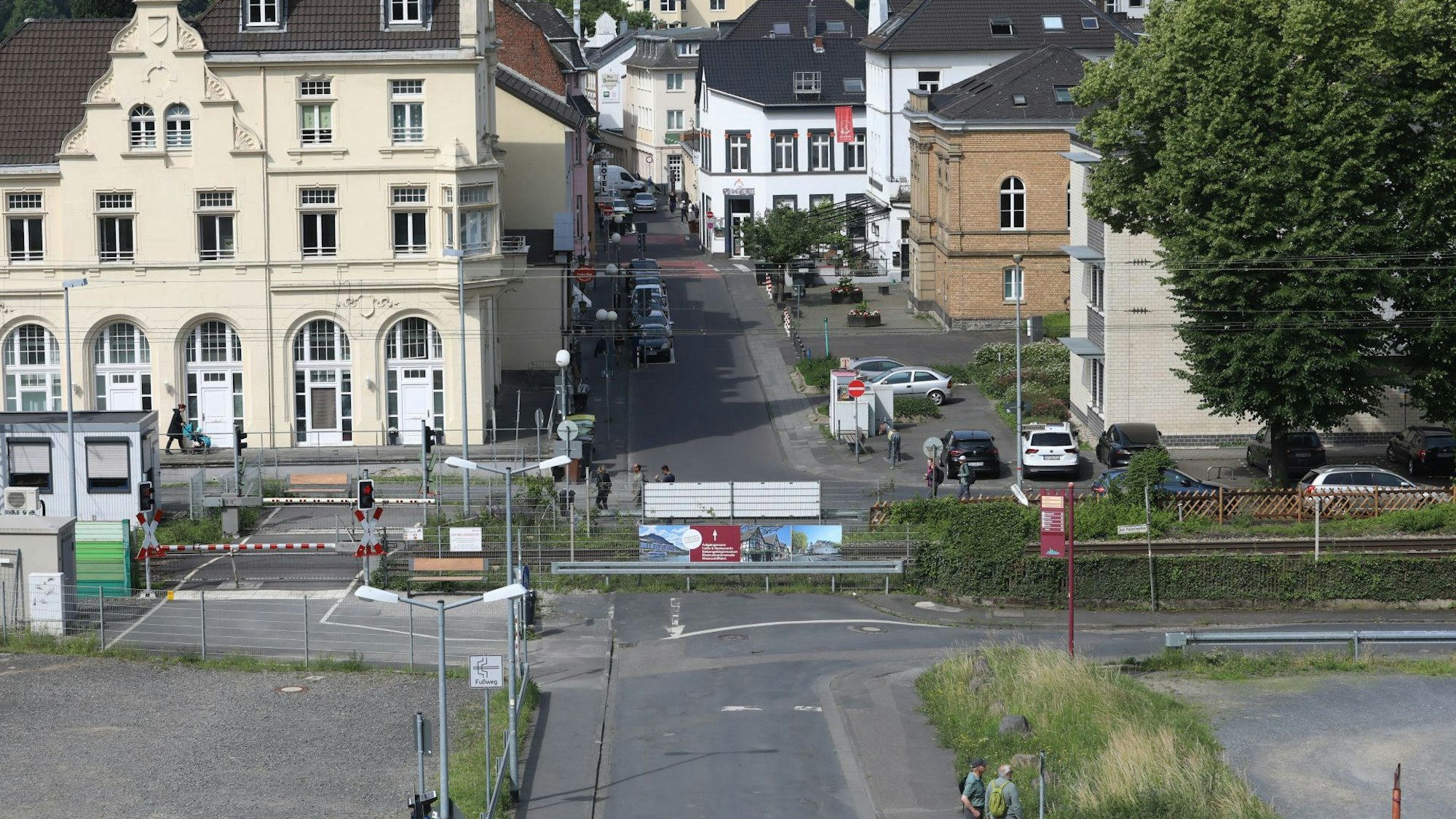 Blick auf eine Straße, die durch eine Bahntrasse geteilt wird. Links sind die Schranken an einem Fußgängerüberweg geschlossen.