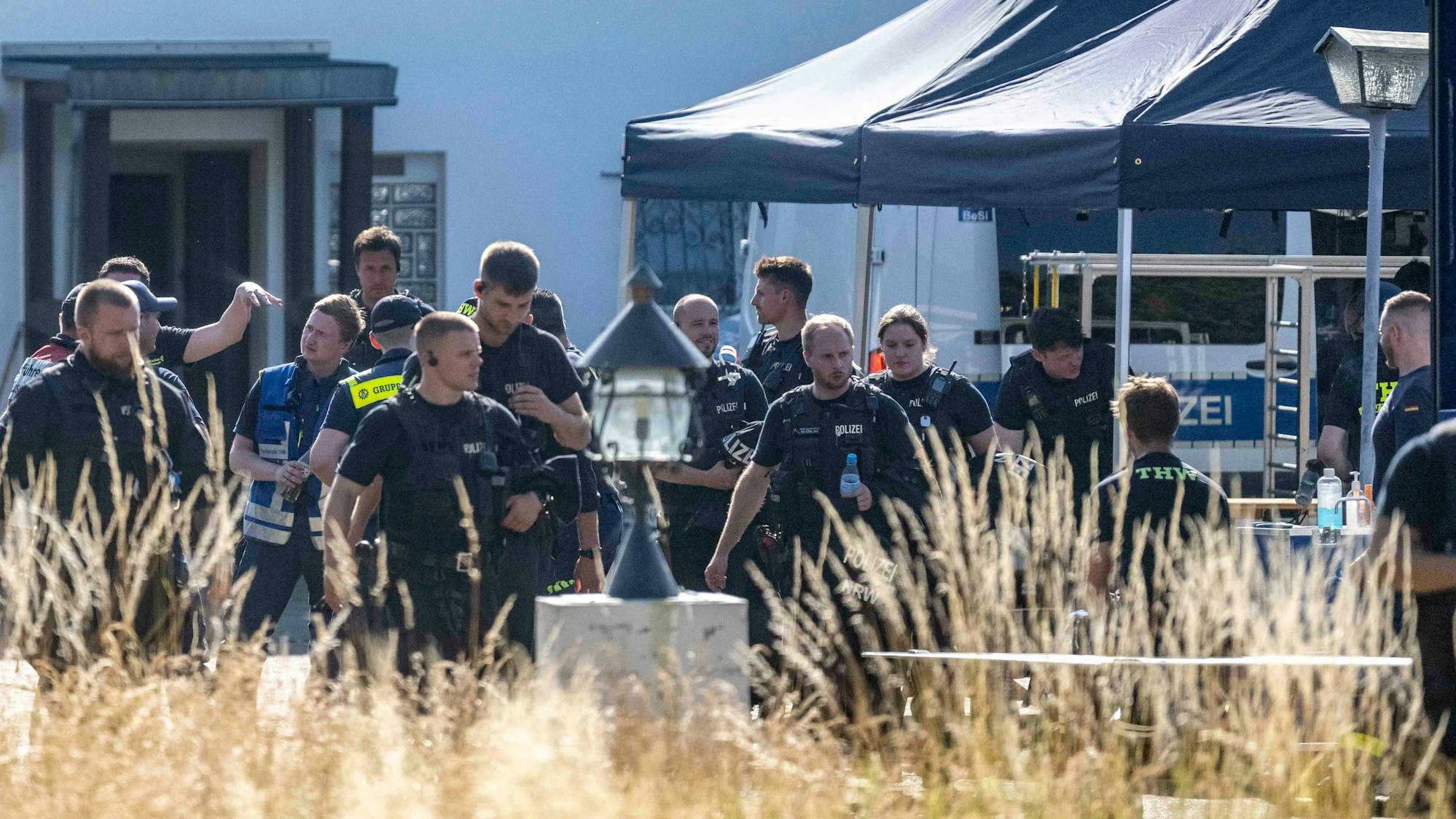 Das Bild zeigt einen Moment während der Razzia. Polizeibeamte und Mitarbeitende des THW befinden sich vor einem Haus.
