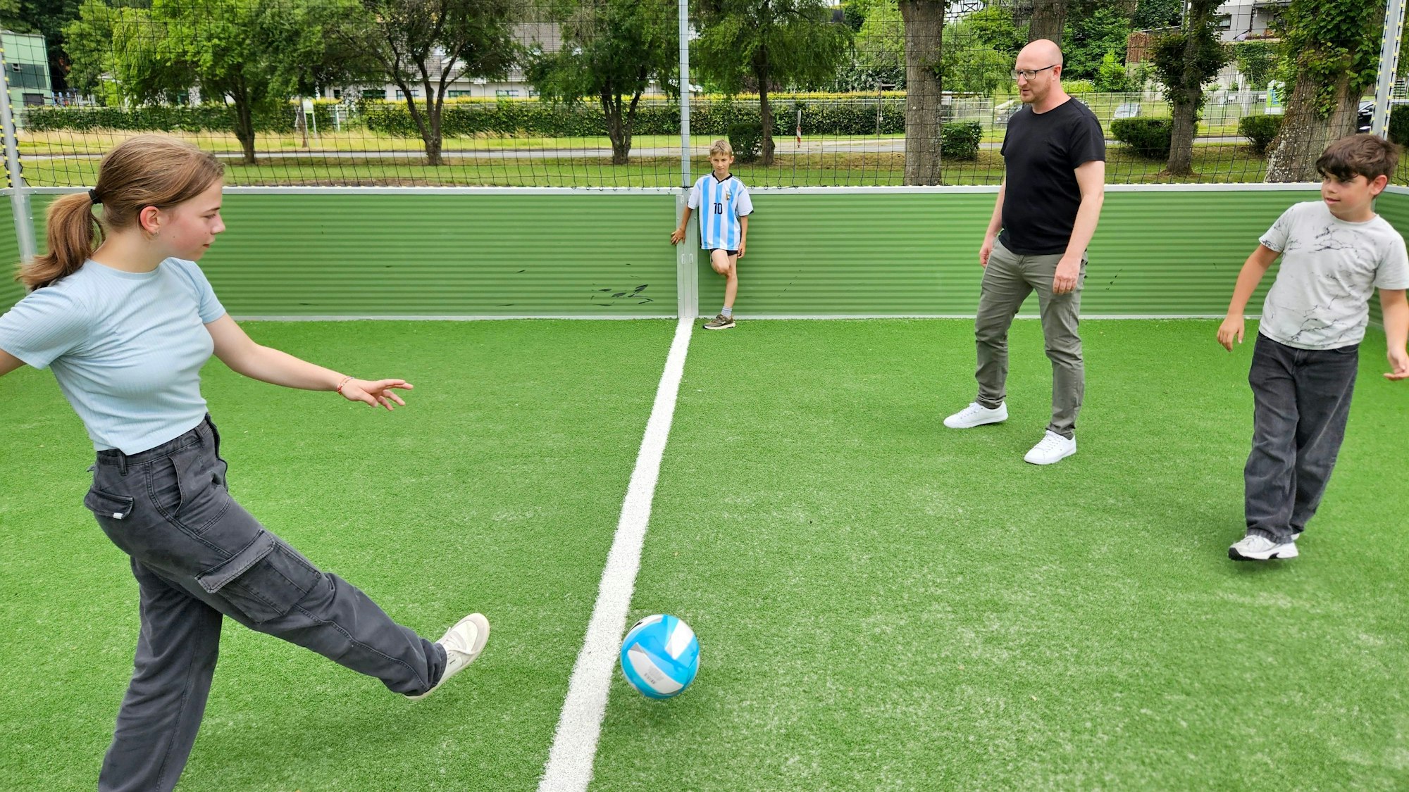 Ein Mädchen und zwei Jungs spielen Fußball mit dem Bürgermeister.