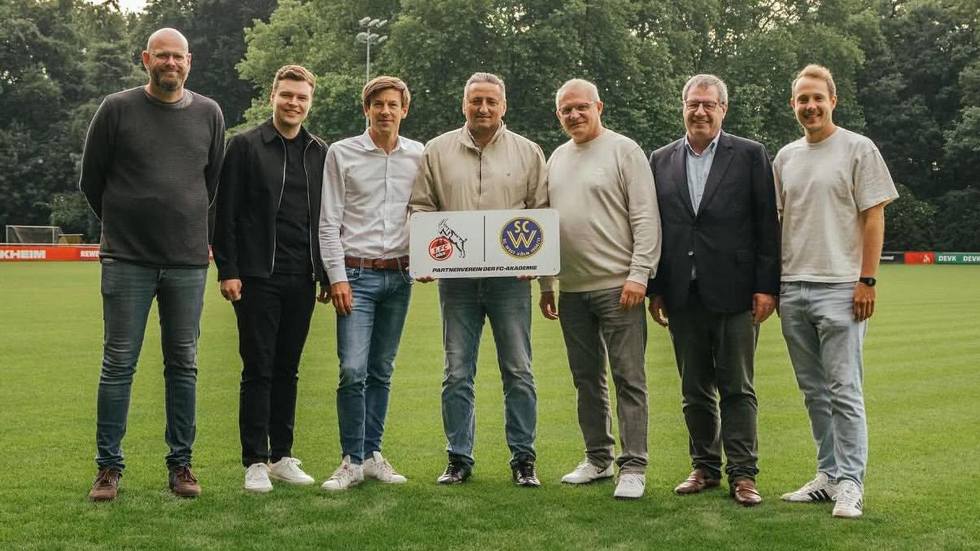 Sieben Männer stehen nebeneinander auf einem Fußballplatz.