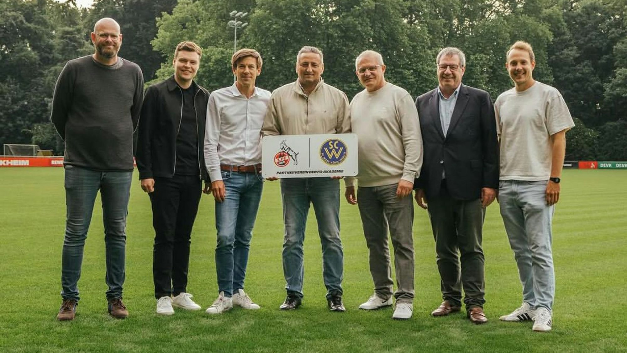 Sieben Männer stehen nebeneinander auf einem Fußballplatz.