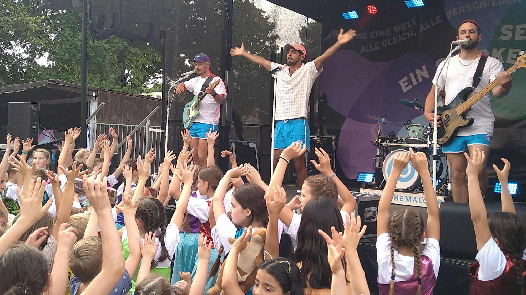 Drei Männer stehen auf der Bühne und singen und spielen Gitarre.