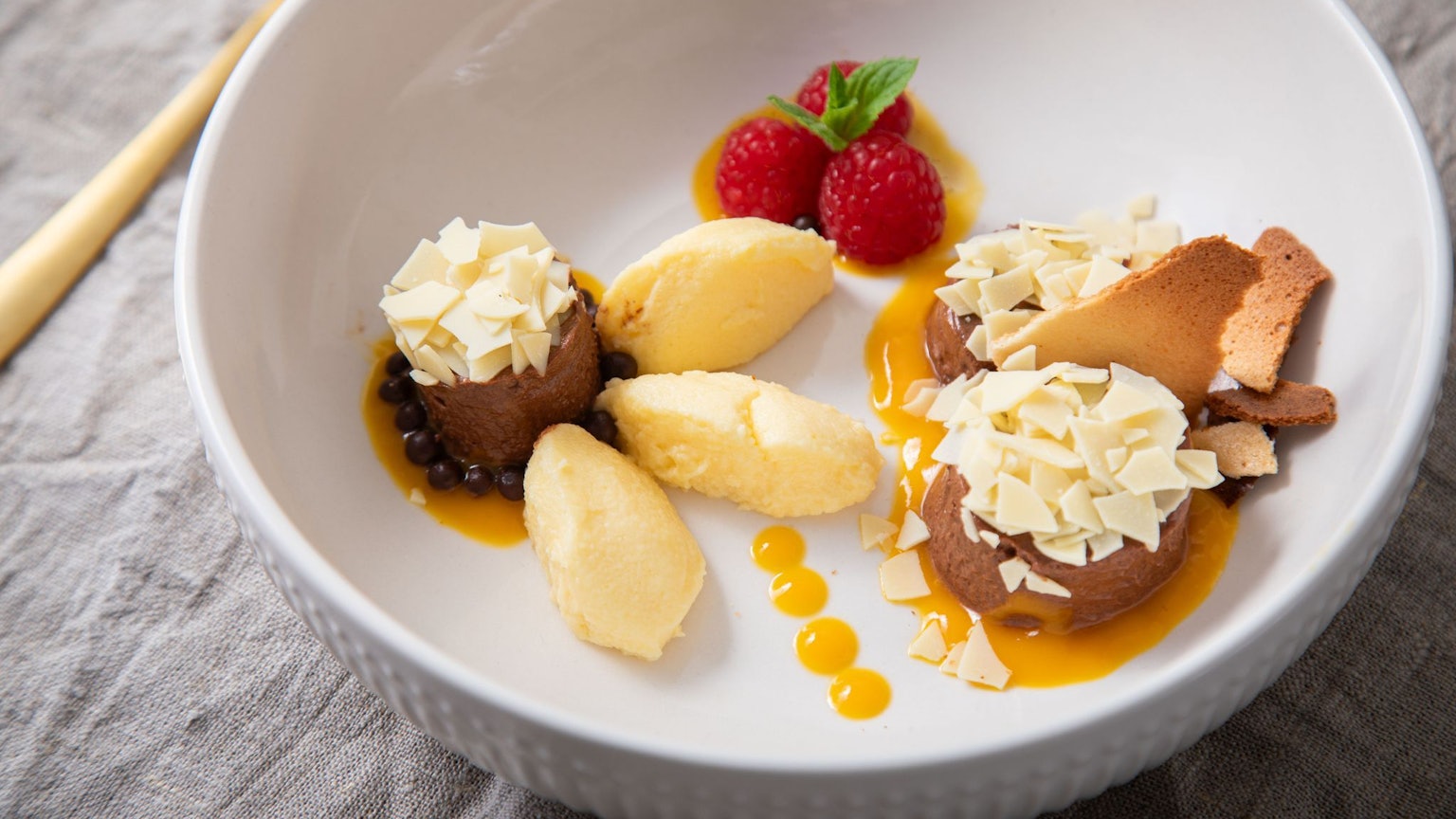 Dessert-Teller mit Schokoladen- und Mango-Mousse auf Mangopüree. Getoppt wird alles mit Eiswaffelsplittern, Schokoraspeln, Himbeeren und Minzblättern.