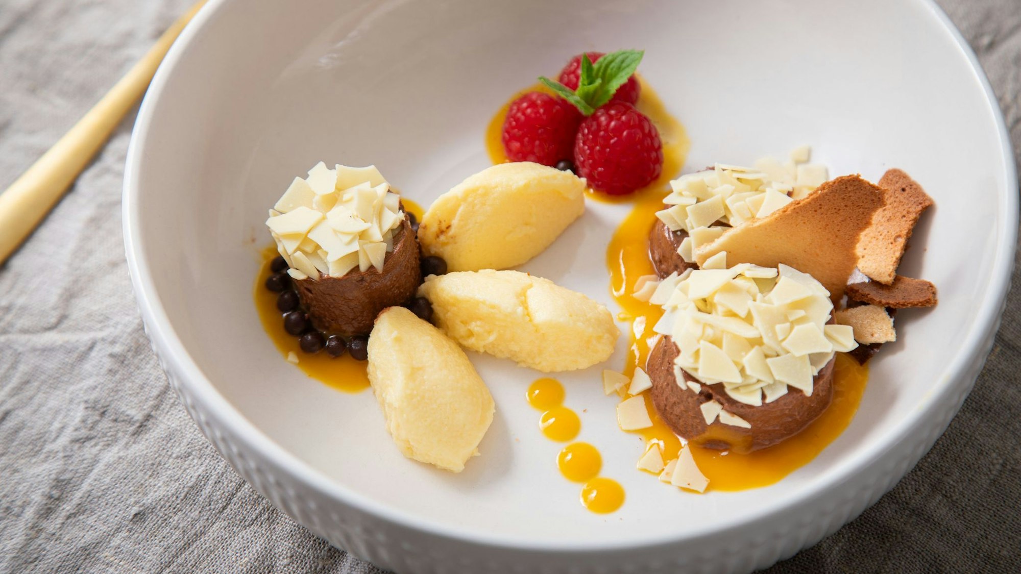 Dessert-Teller mit Schokoladen- und Mango-Mousse auf Mangopüree. Getoppt wird alles mit Eiswaffelsplittern, Schokoraspeln, Himbeeren und Minzblättern.