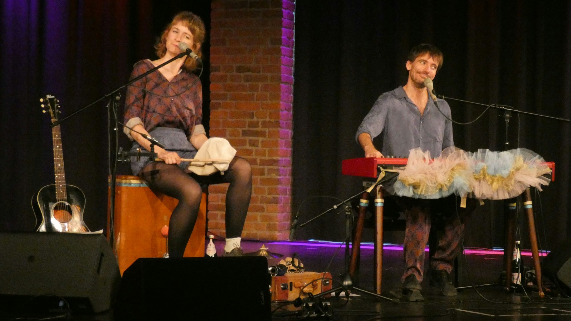 Ein Kabarett-Duo, bestehend aus einer Frau und einem Mann, führt auf einer Bühne ihr Programm vor.