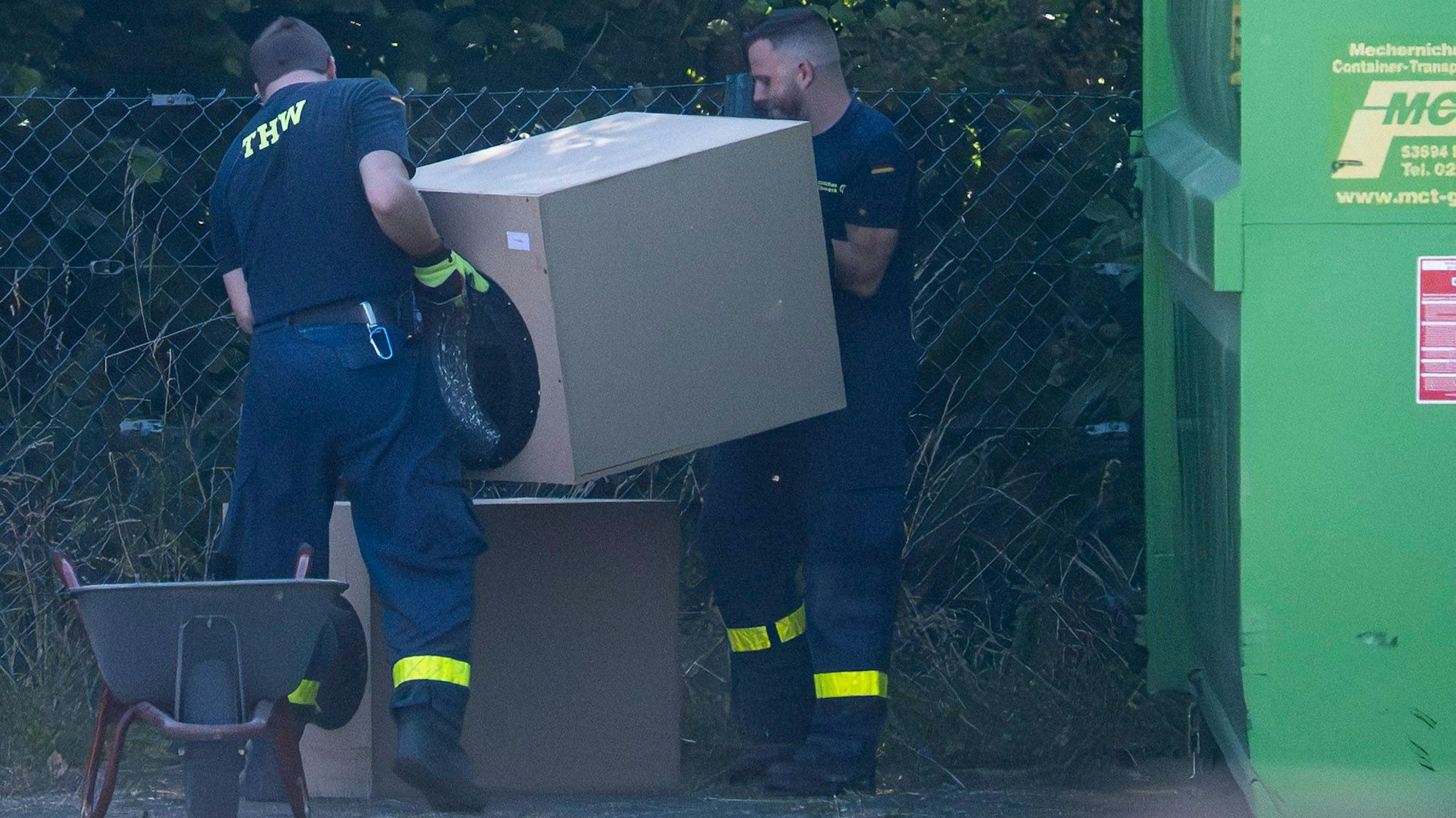 Das Bild zeigt zwei Mitarbeiter des THW, wie sie eine Holzbox auf eine andere Stellen.