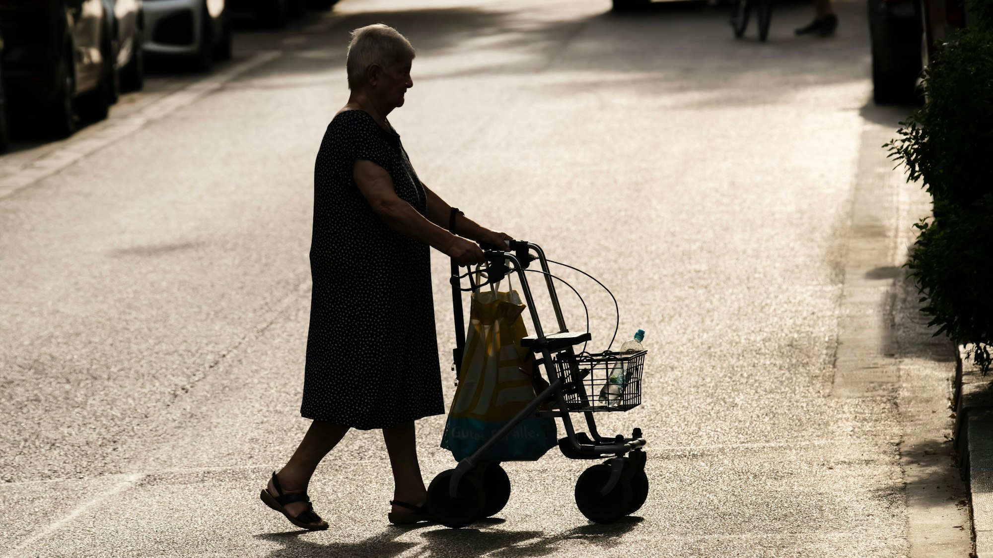 Eine alte Frau mit Rollator ist bei Sommerhitze in der Stadt unterwegs.