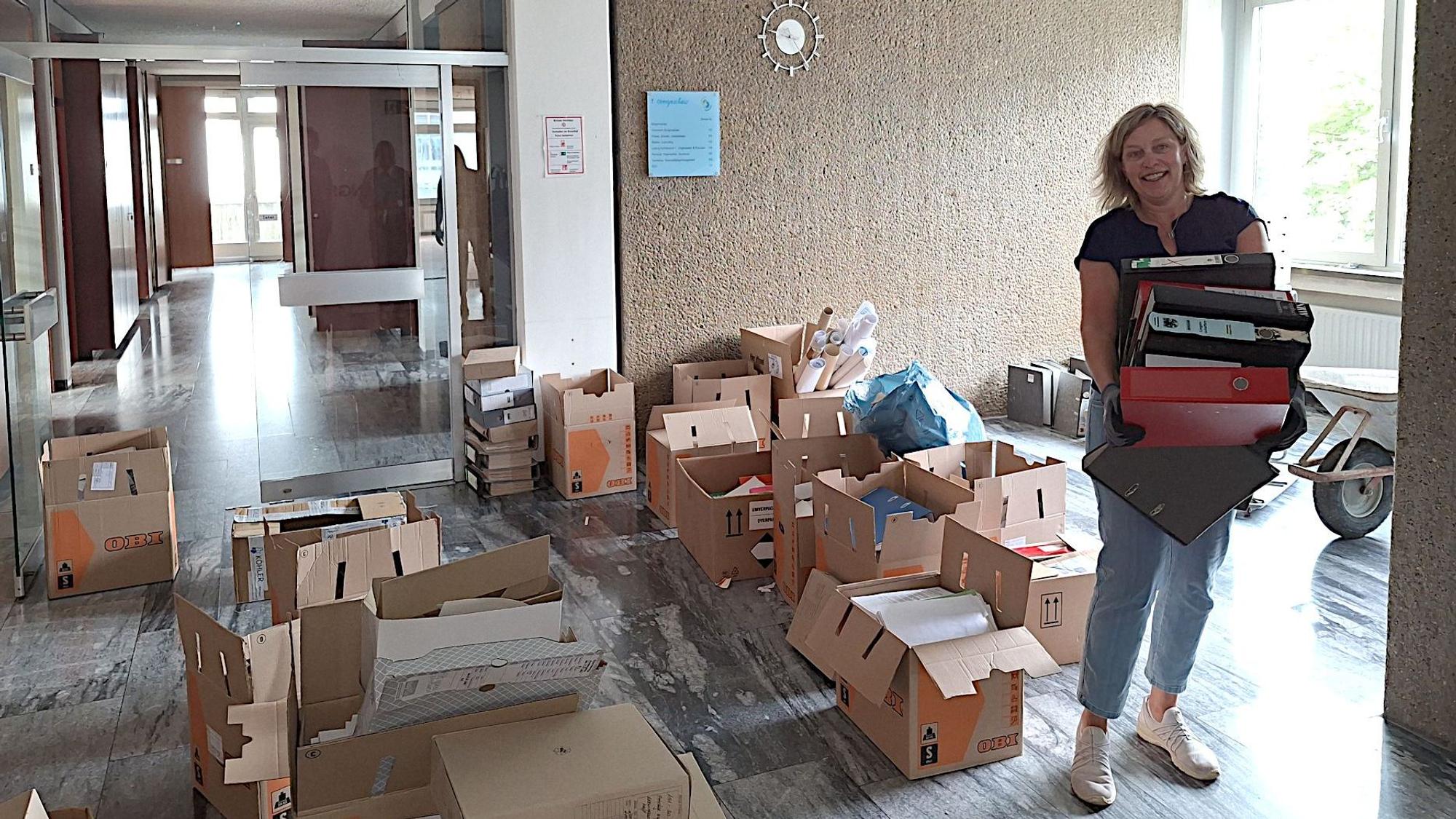 Michaela Bell trägt einige Aktenordner. Um sie herum im alten Rathaus von Blankenheim stehen Umzugskisten.