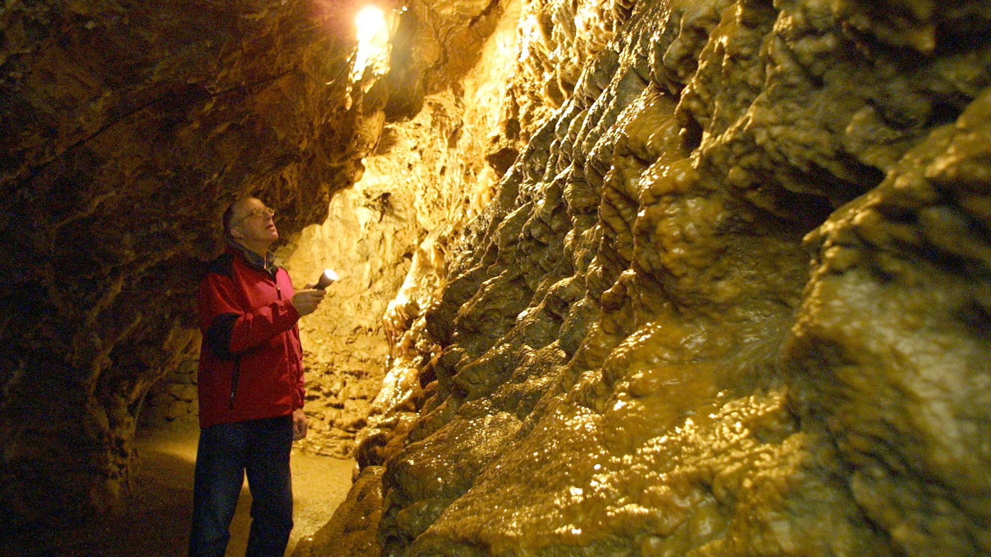 Ein Mann steht in einer Tropfsteinhöhle und leuchtet mit einer Taschenlampe.