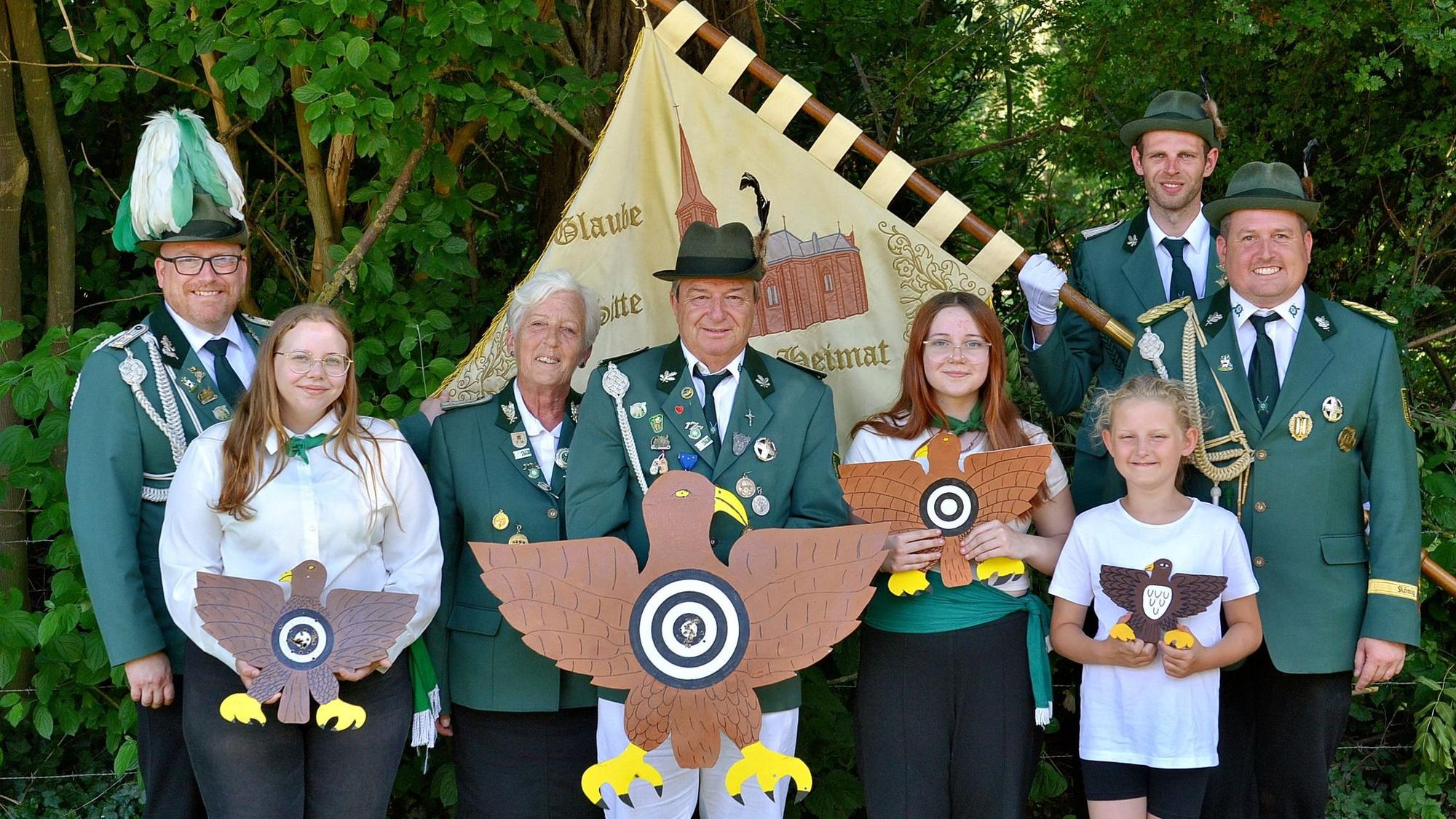 Schützenbrüder und -schwestern stehen mit ihren Trophäen in einer Reihe, hinter ihnen weitere Vereinsmitglieder. Ein Mann hält die Fahne der Bruderschaft.