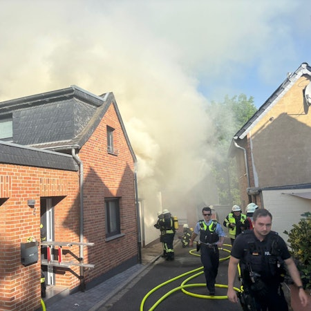 Das Bild zeigt mehrere Einsatzkräfte von Feuerwehr und Polizei an einem qualmenden Gebäude