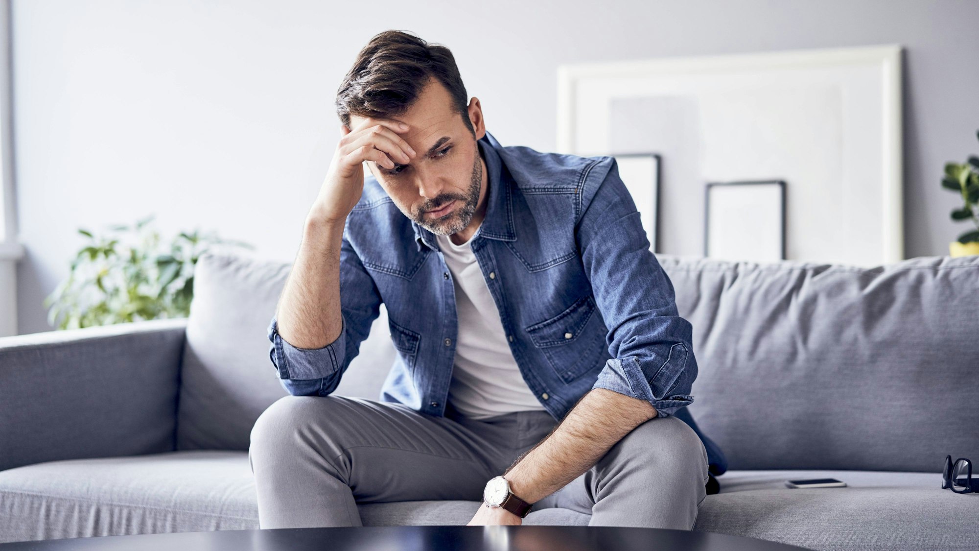 Mann sitzt nachdenklich traurig auf der Couch.