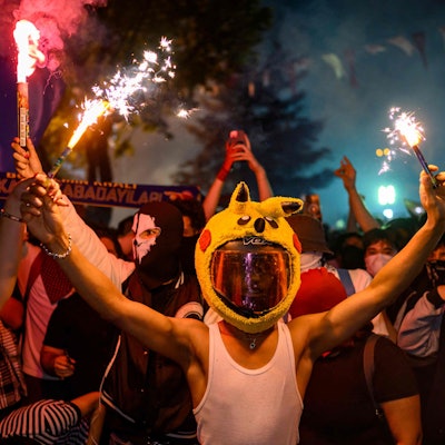 A protester in a pikachu hat holds a firecracker during a rally protesting the 100th day of the detention of Istanbul Mayor Ekrem Imamoglu, at Sarachane Square in Istanbul, on July 1, 2025. (Photo by Yasin AKGUL / AFP)