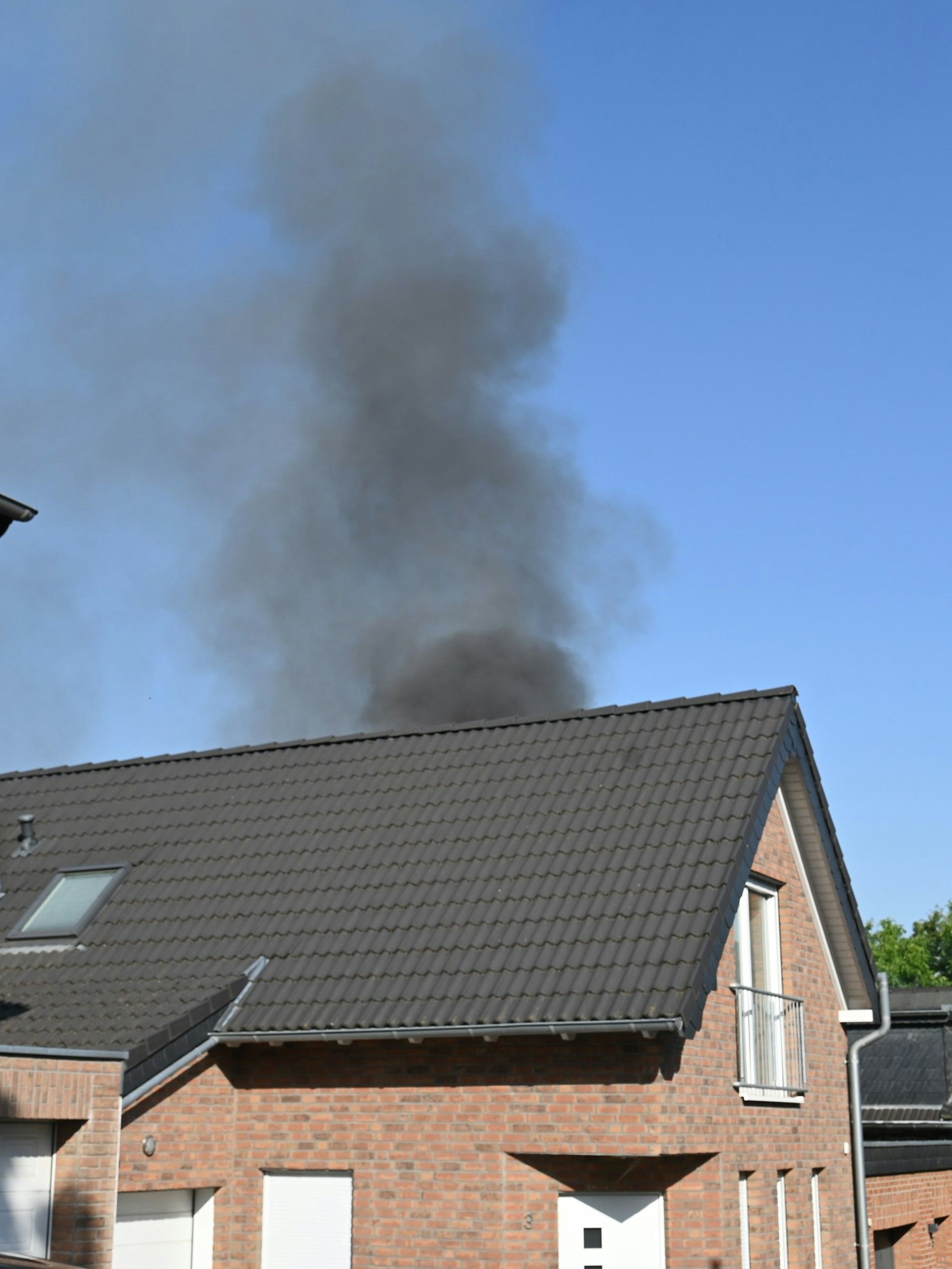 Das Bild zeigt eine Wohnhaus und eine schwarze Rauchsäule im Hintergrund