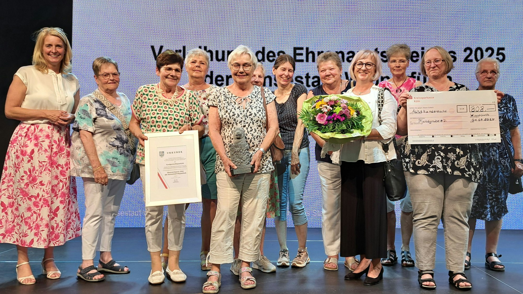 Elf Damen der Fundgrube und Bürgermeisterin Anne Loth stehen auf einer Bühne.