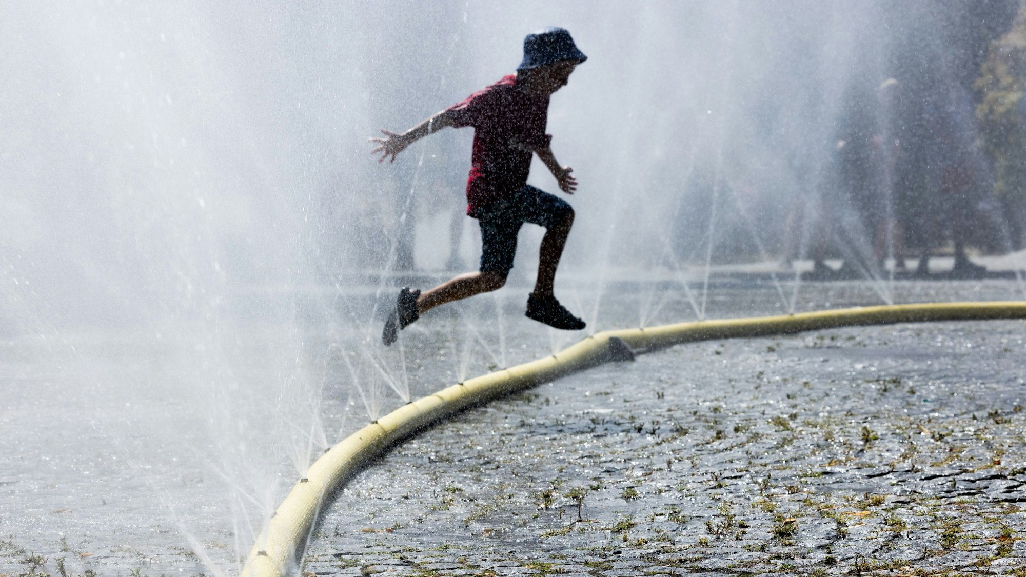 Ein Junge springt über einen perforierten Feuerwehrschlauch.