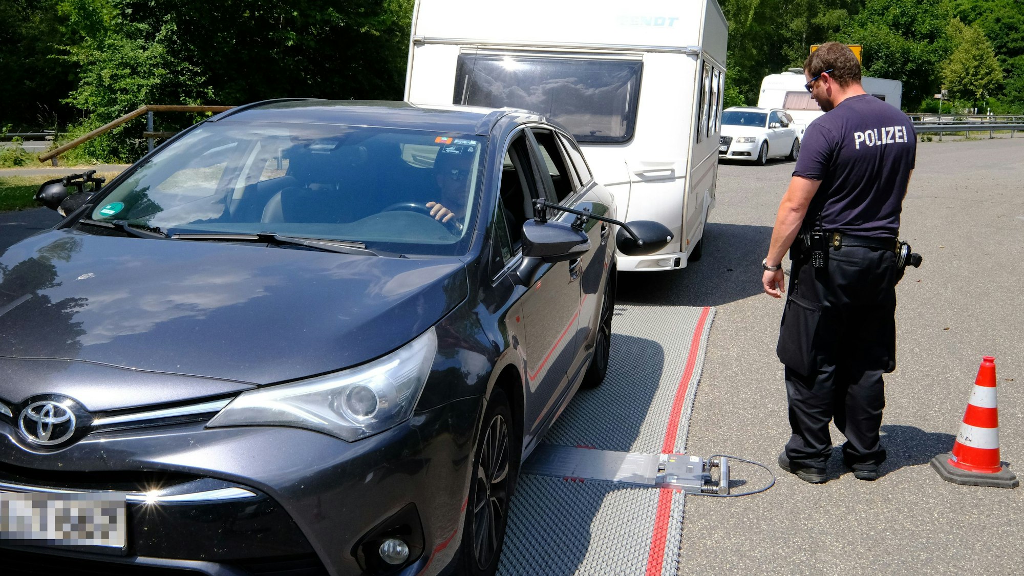 Ein Wohnwagengespann bei der Überfahrt einer mobilen Fahrzeugwaage. Rechts davon steht ein Polizist.