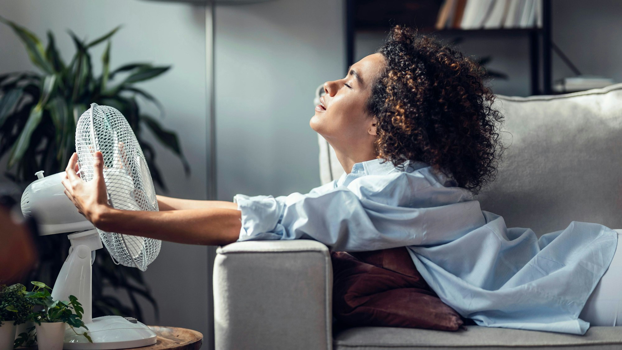 Eine Frau nutzt einen Ventilator, um sich an einem heißen Tag zuhause angenehm abzukühlen. (Symbolbild)