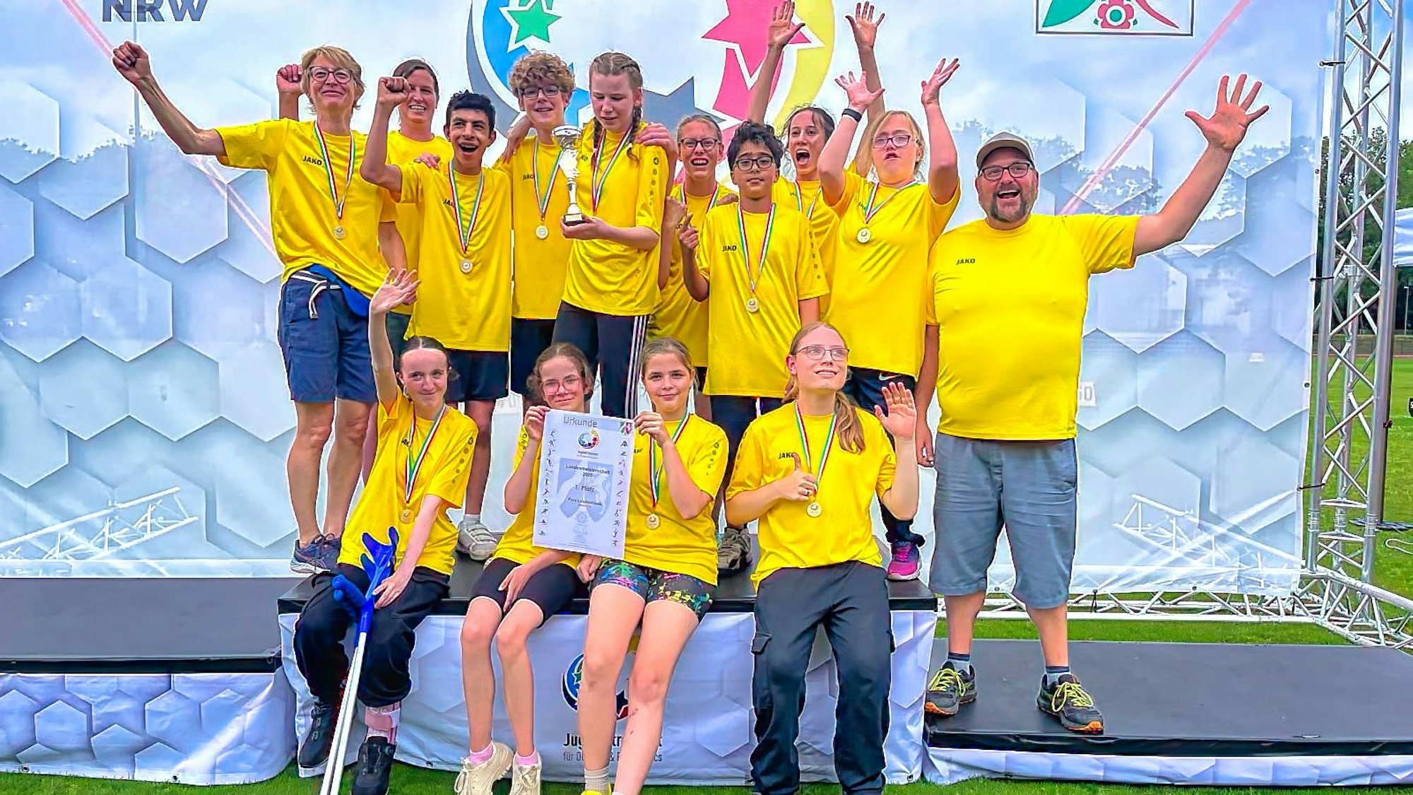 Schüler in gelben T-Shirts sitzen auf einem Treppchen.