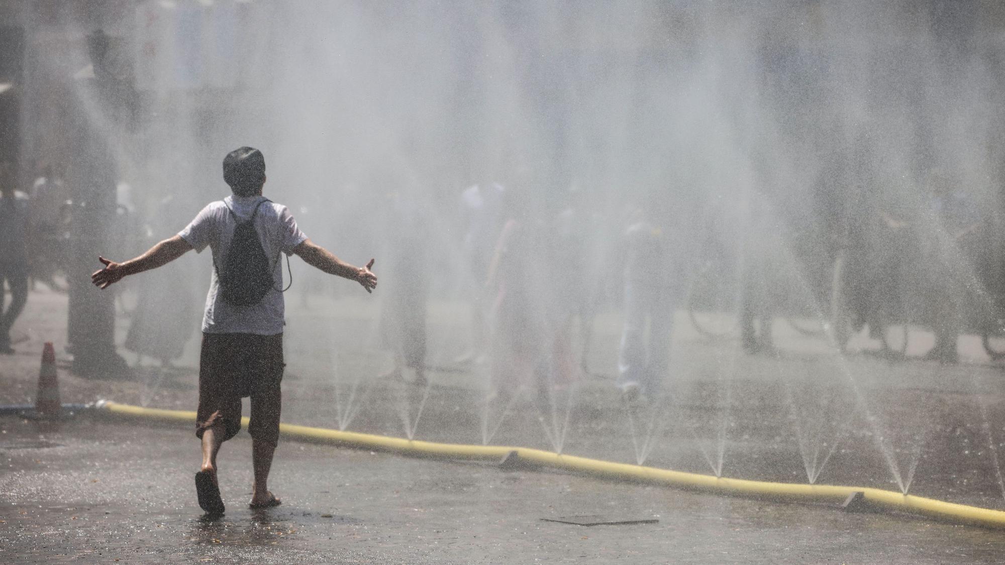 Ein Mann geht durch den Wassernebel in der Südstadt. Unter dem Motto „Cooling Cologne“ bietet die Stadt Köln in der Südstadt die Möglichkeit für eine Abkühlung mit Schläuchen an, die feinen Wassernebel versprühen.