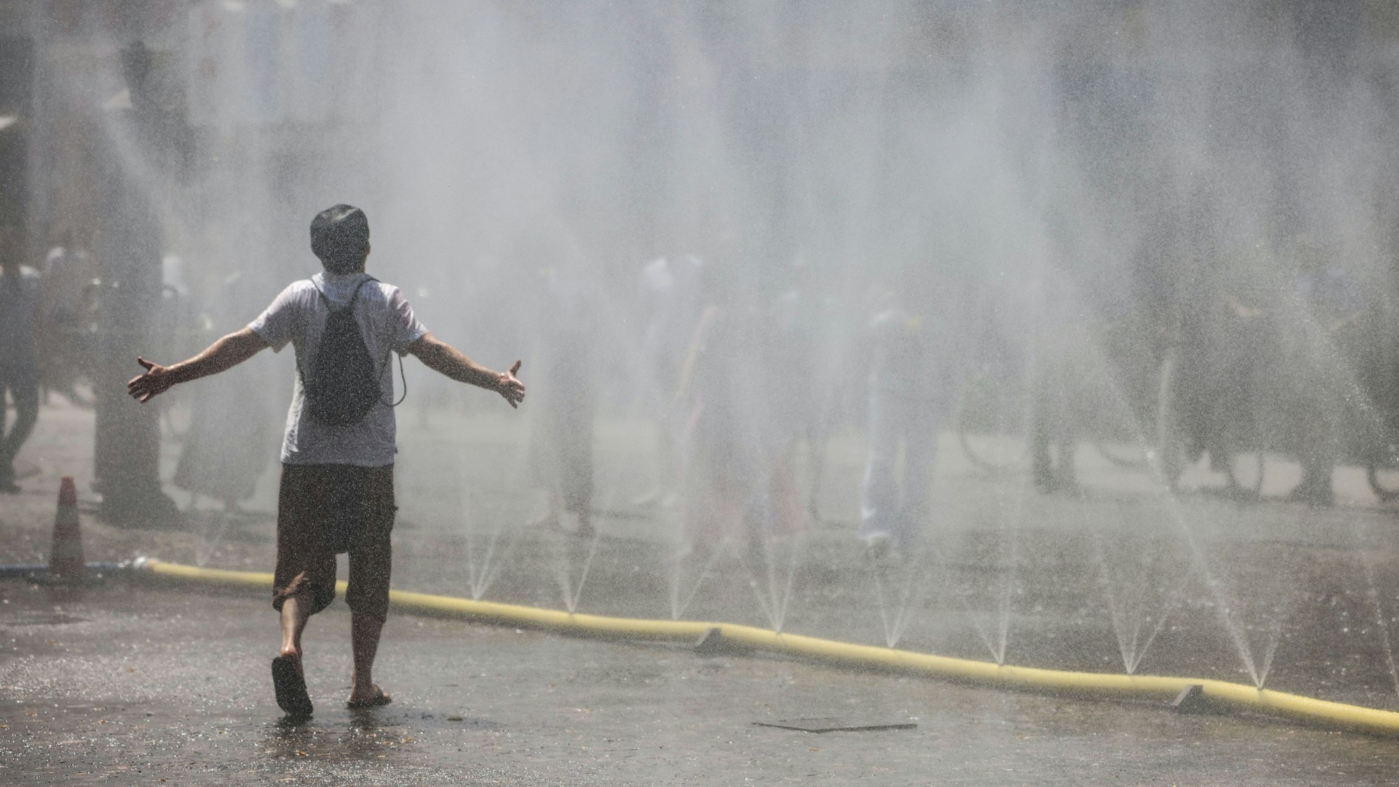 Ein Mann geht durch den Wassernebel in der Südstadt. Unter dem Motto „Cooling Cologne“ bietet die Stadt Köln in der Südstadt die Möglichkeit für eine Abkühlung mit Schläuchen an, die feinen Wassernebel versprühen.