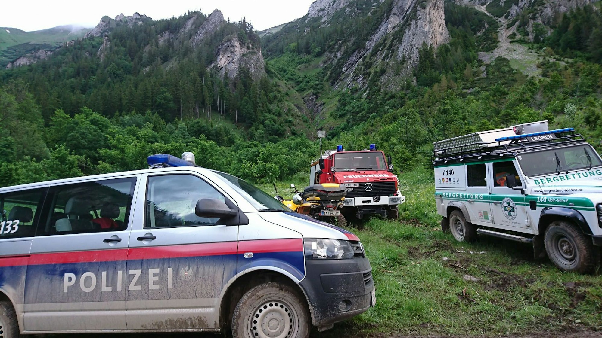 Einsatzfahrzeuge von Polizei, Feuerwehr und Bergrettung stehen am Berg.