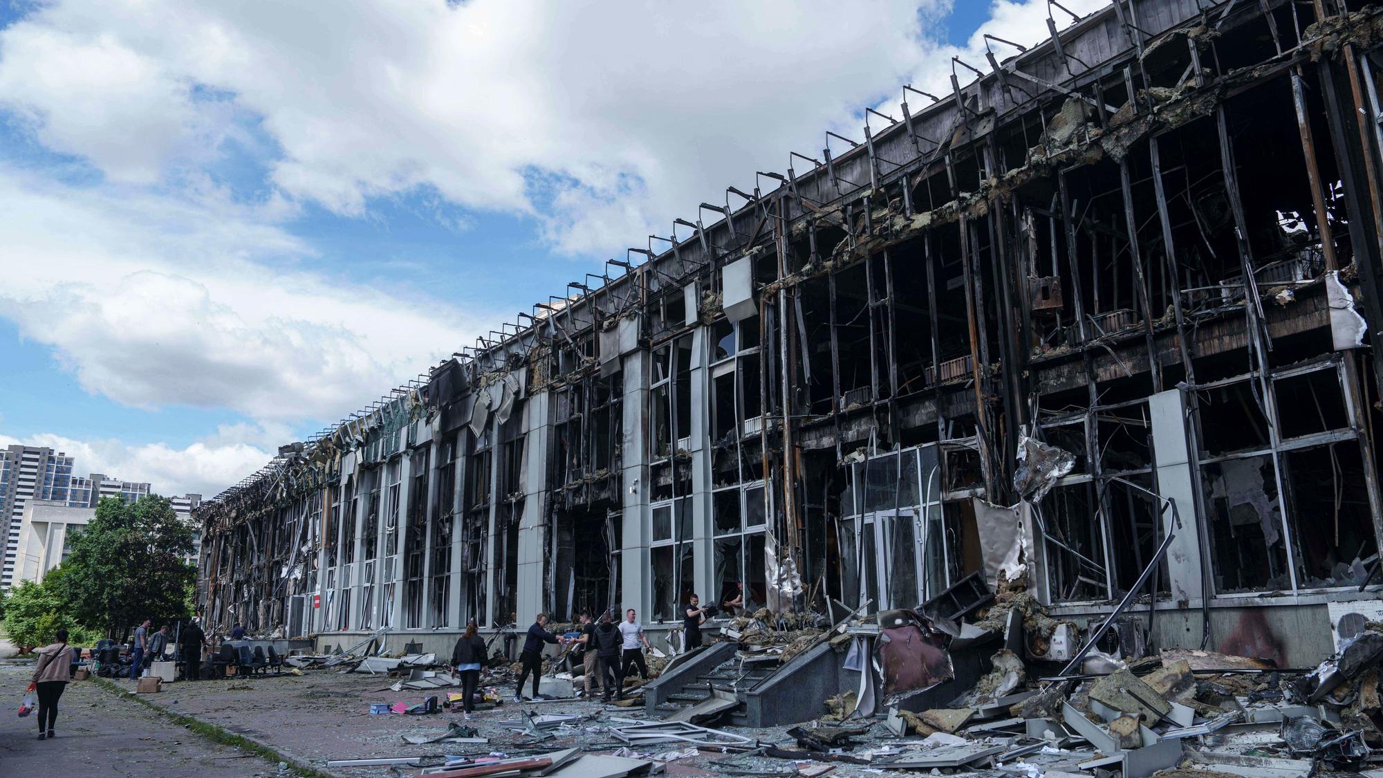 ARCHIV - 23.06.2025, Ukraine, Kiew: Menschen transportieren Habseligkeiten aus einem durch einen russischen Angriff zerstörten Bürogebäude in Kiew. (zu dpa: «Ukraine: UN-Generalsekretär für bedingungslose Waffenruhe») Foto: Evgeniy Maloletka/AP/dpa +++ dpa-Bildfunk +++