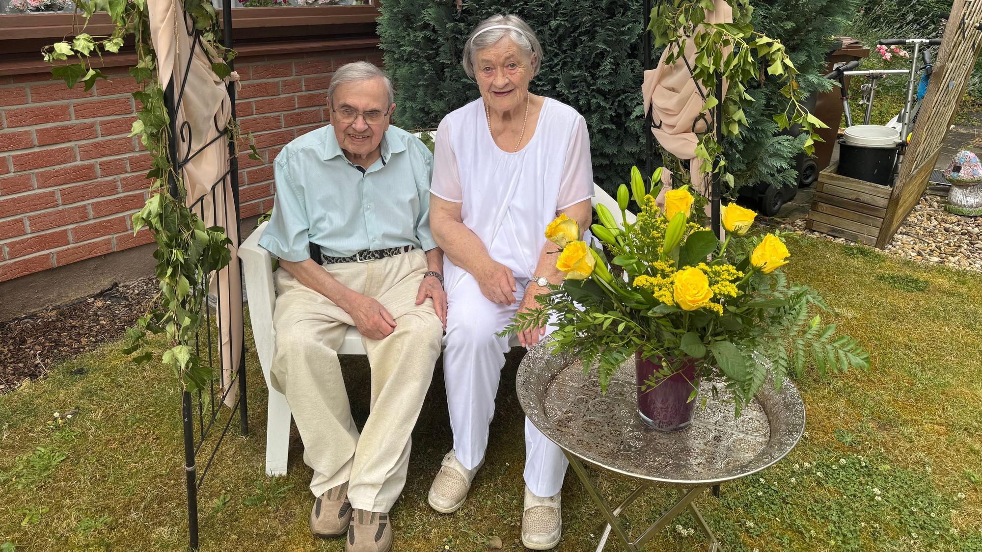 Ein älteres Ehepaar sitzt auf einer Bank im Garten.