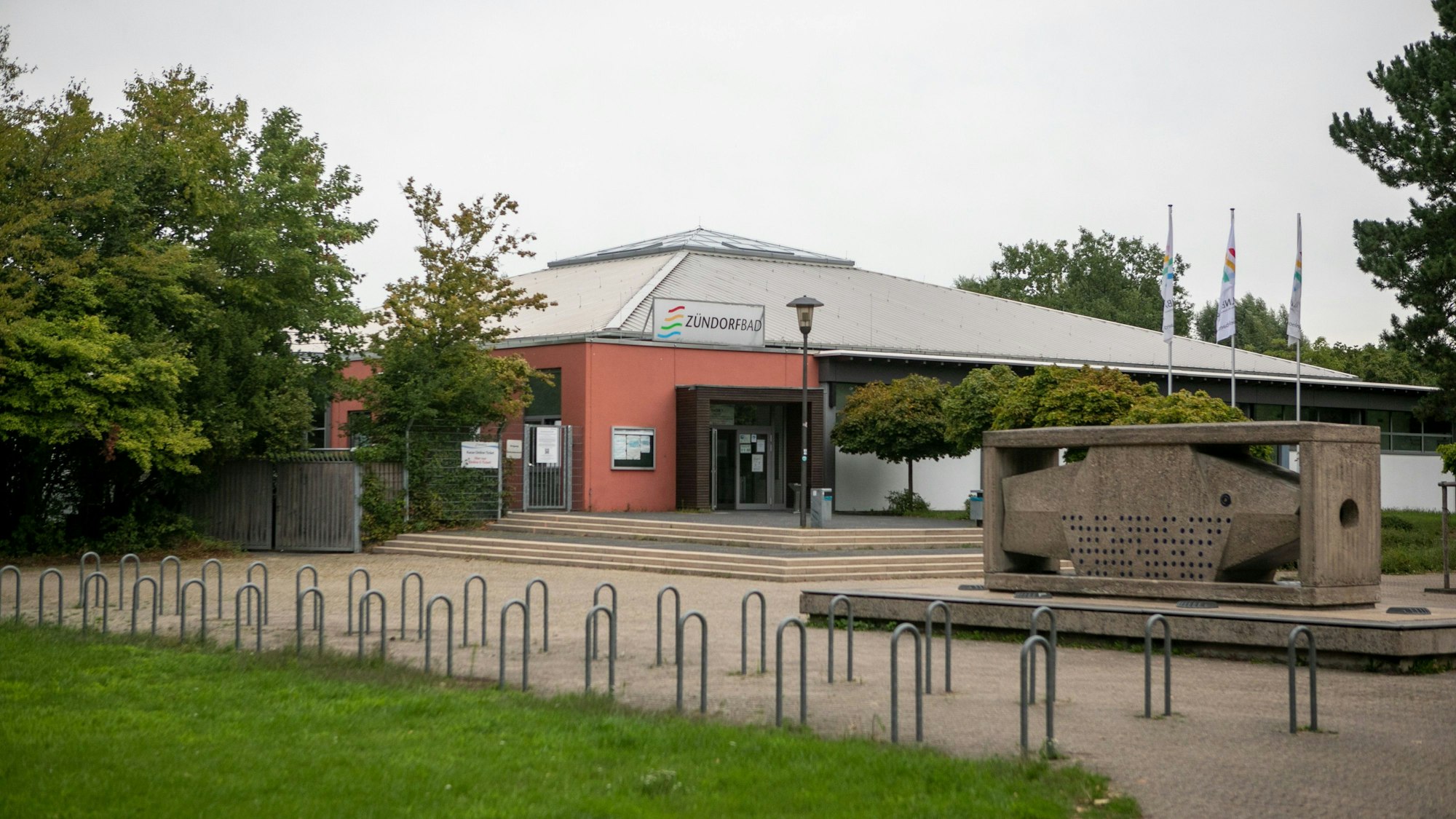 Das Zündorfbad ist ein großes Gebäude mit roter Fassade und einem langgezogenen Dach.