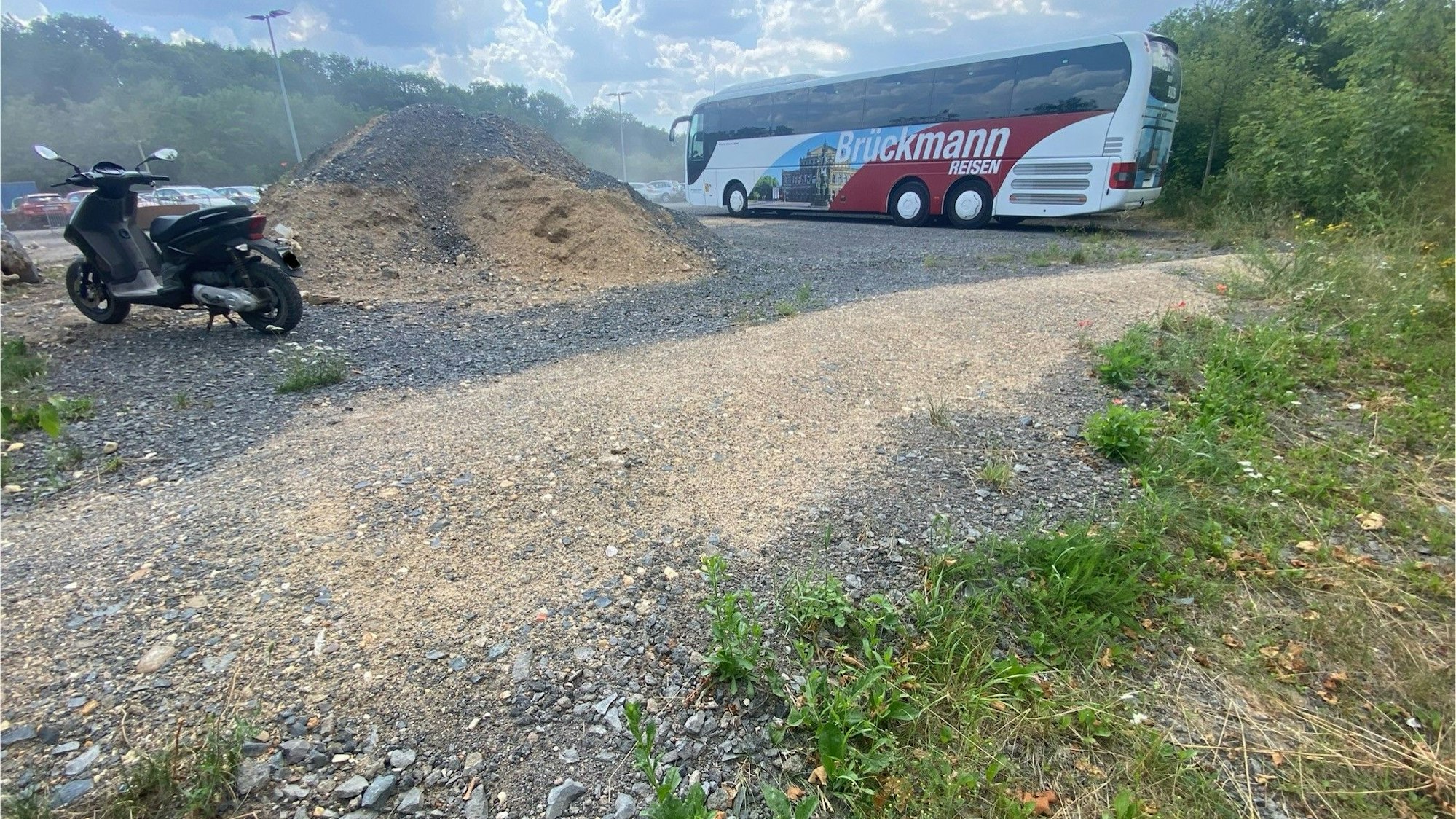 Zu sehen ist ein kleiner Wall aus Schotter und Sand, im Hintergrund steht ein Reisebus.
