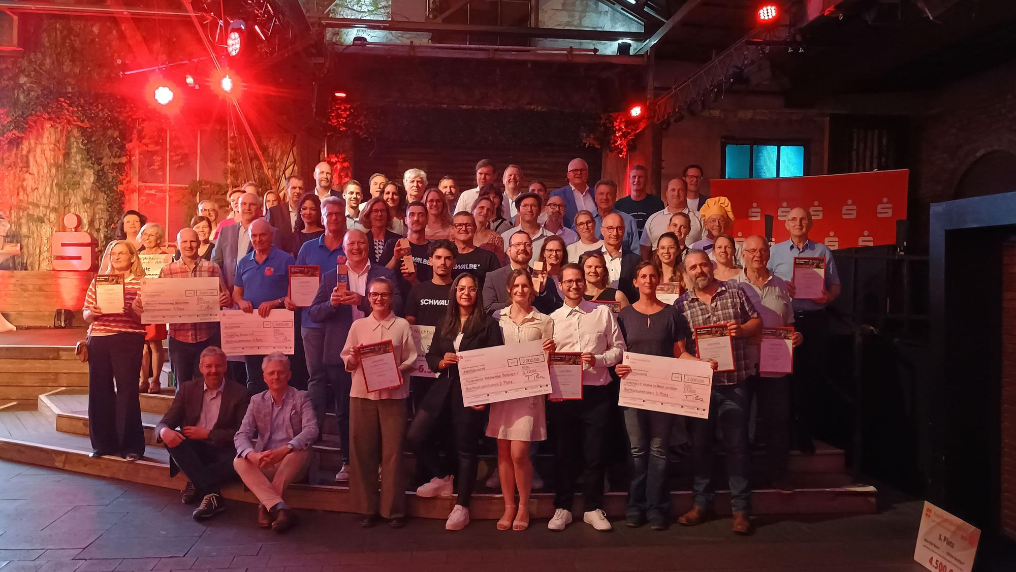 Das Bild zeigt zahlreiche Menschen aus den Vereinen und Betrieben, die mit Schecks und Urkunden für ein Gruppenfoto posieren.