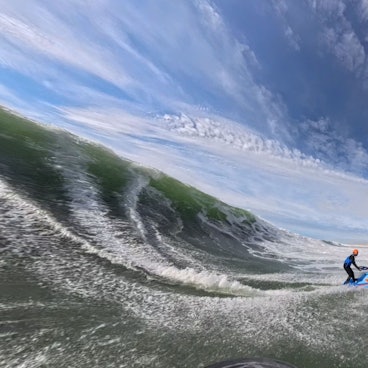 Zu sehen ist eine Jetski-Fahrerin mitten in einer riesigen Welle.