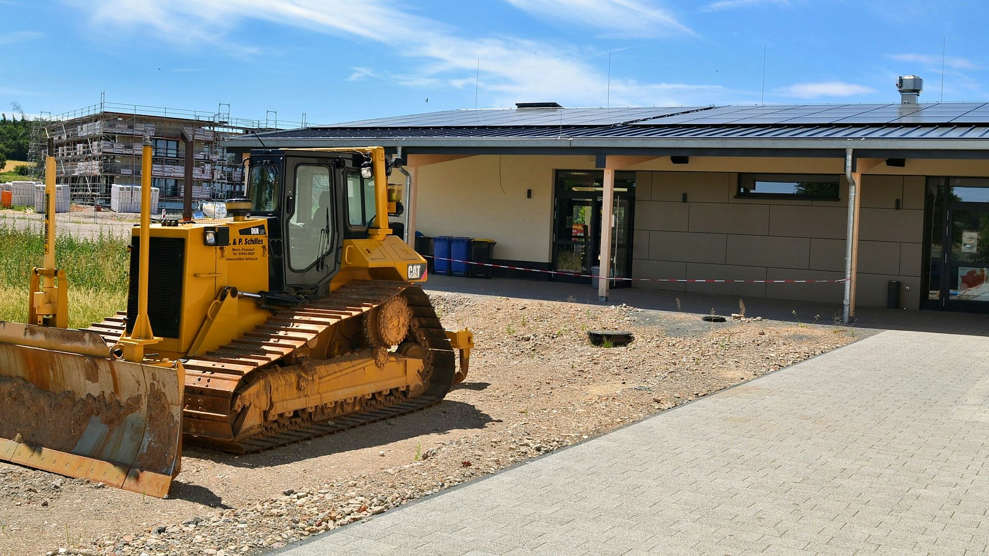 Eine Planierraupe steht auf einem Schotterplatz vor einem Gebäude.