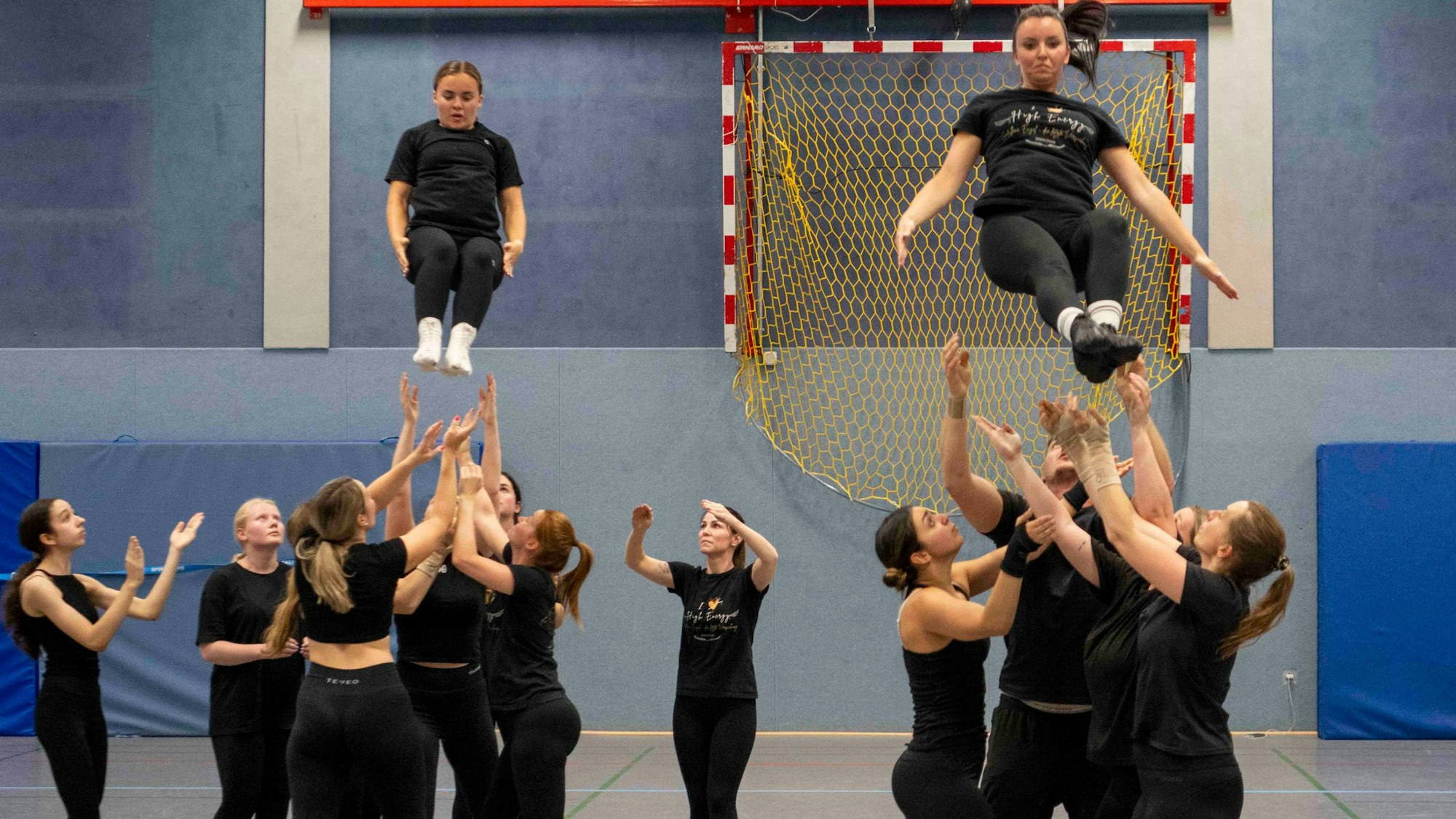 Das Bild zeigt, wie zwei Hebefiguren aufgelöst werden. Zwei Tänzerinnen springen in die Arme ihrer Mannschaftskollegen.