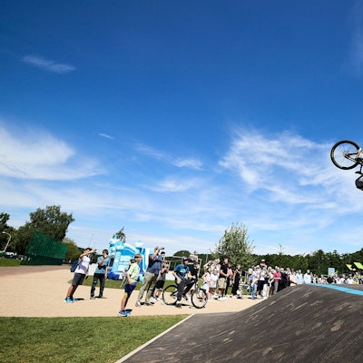 Lennox Zimmermann macht mit seinem BMX-Bike einen Salto in der Luft, am Boden steht eine Schar Zuschauer.