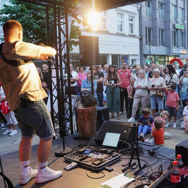 Das Bild zeigt den Singer-Songwriter auf der Bühne, im Hintergrund zahlreiche Gäste in der Innenstadt.