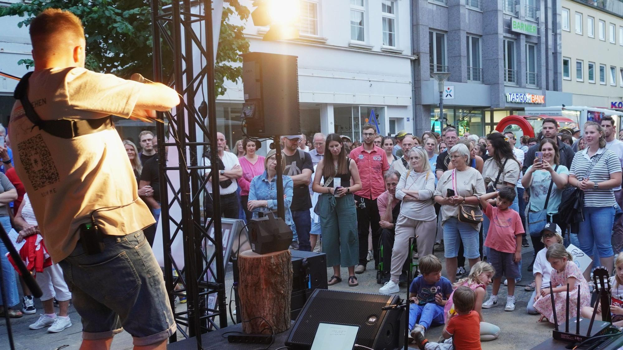 Das Bild zeigt den Singer-Songwriter auf der Bühne, im Hintergrund zahlreiche Gäste in der Innenstadt.