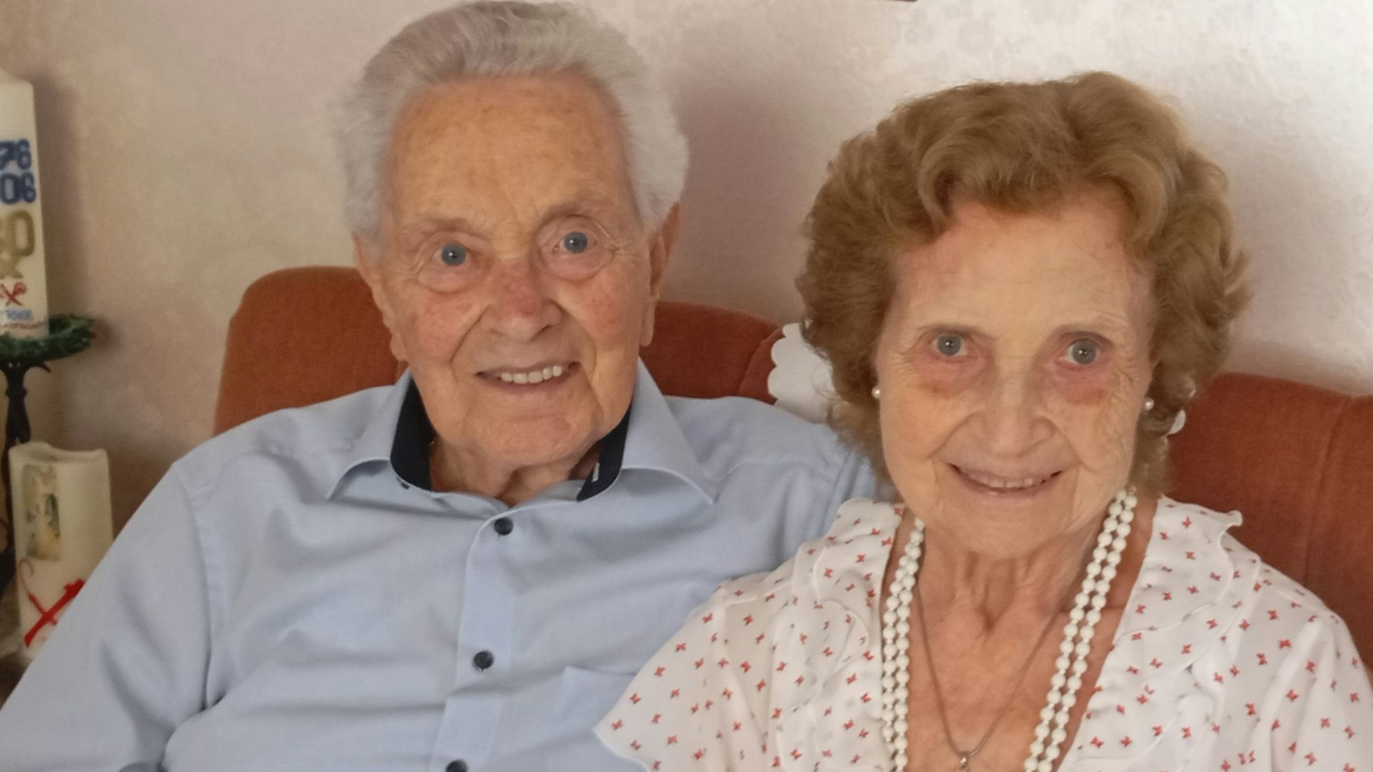 Ein älteres Ehepaar sitzt auf einem Sofa, die Frau und der Mann lächeln in die Kamera.