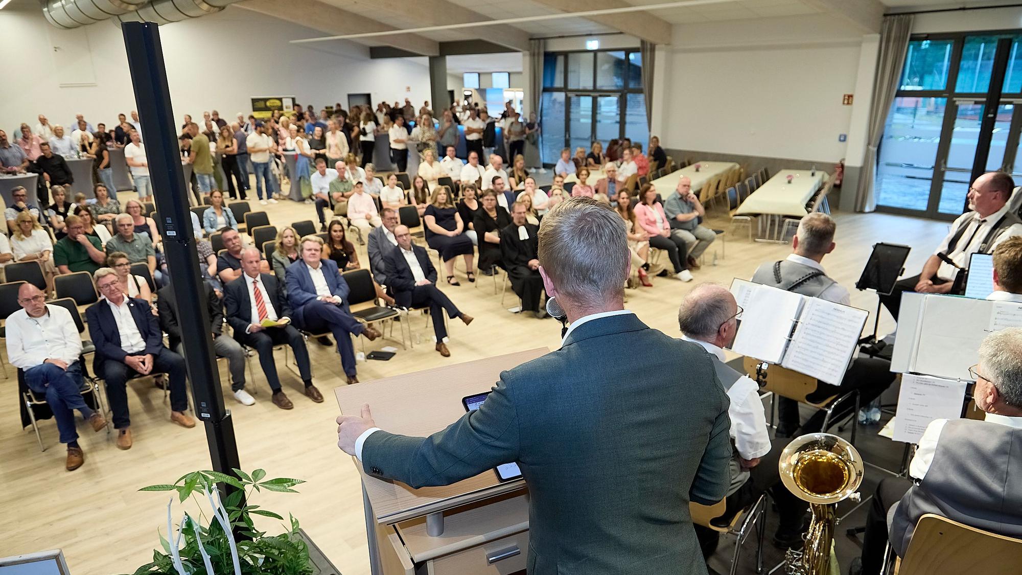Markus Ramers steht an einem Rednerpult und spricht zu einem Publikum, das auf Stühlen vor einer Bühne sitzt.