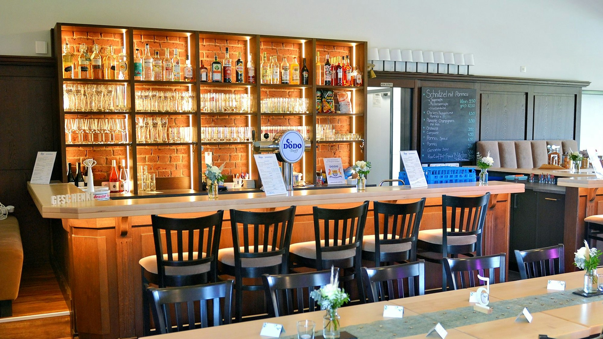 Das Bild zeigt eine moderne Theke mit beleuchteten Regalen und Barhockern.