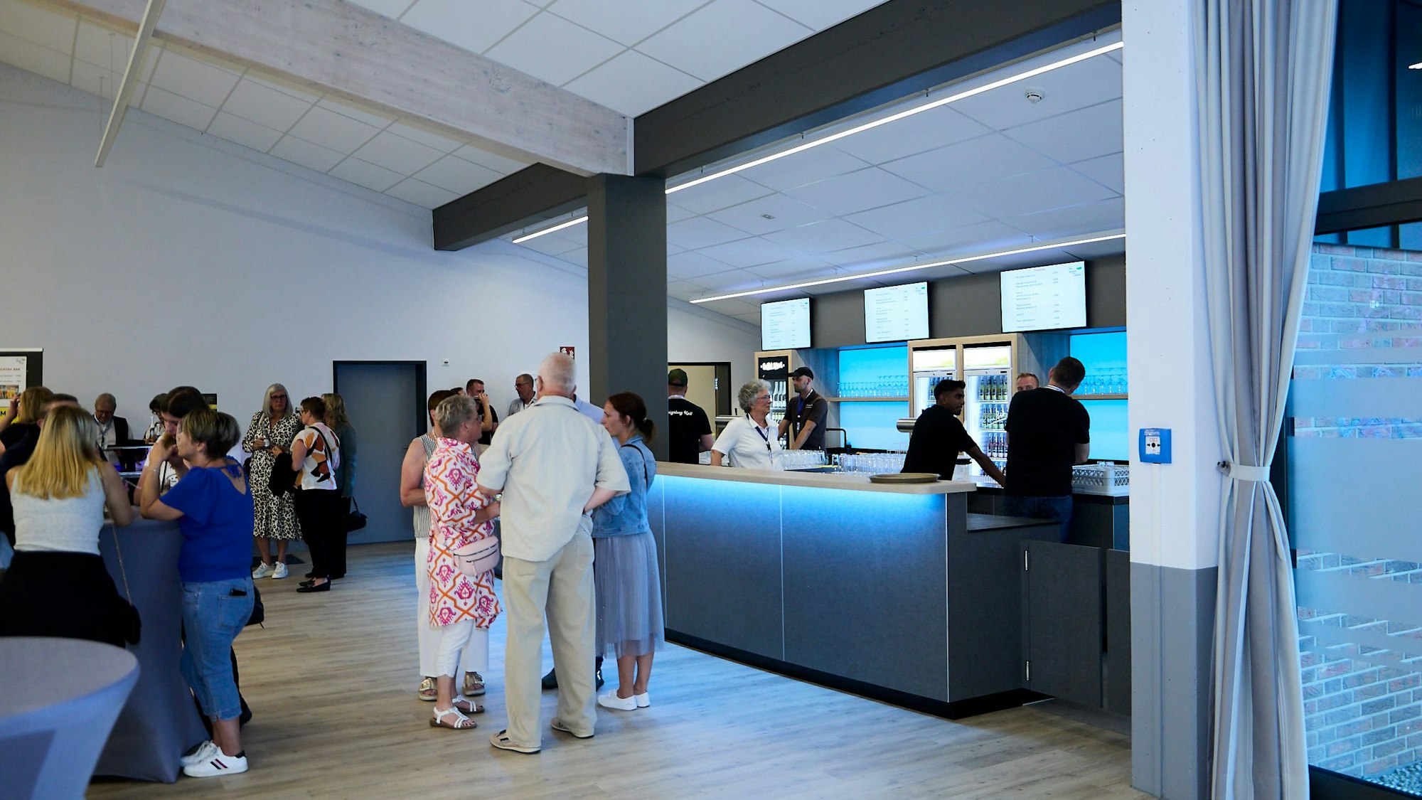 Menschen stehen vor und an einer grauen, modernen und beleuchteten Theke.