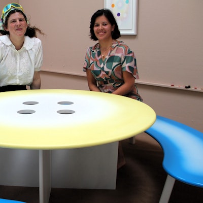 Zwei junge Frauen sitzen an einem runden Tisch, der vier Löcher hat.