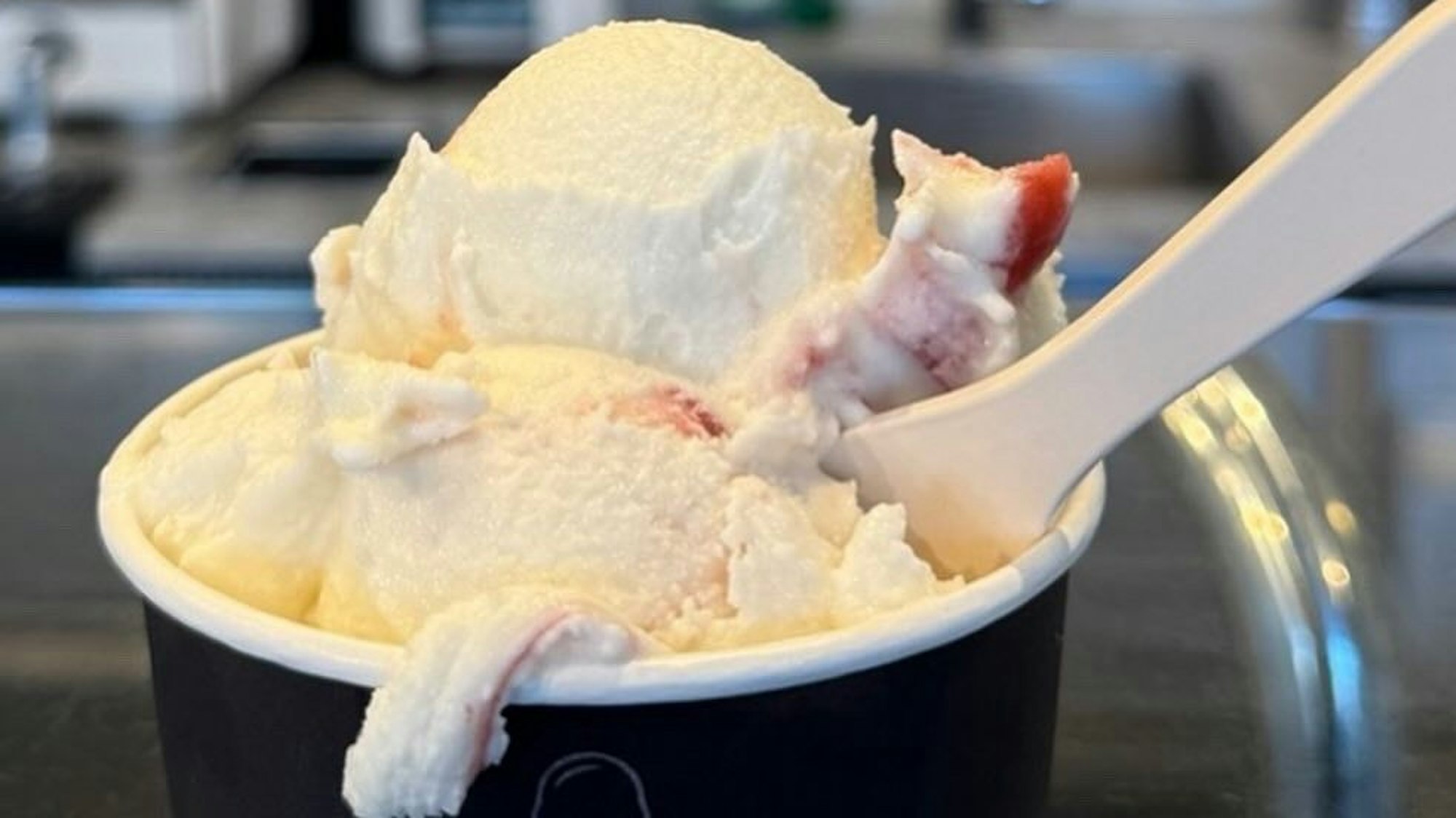 Eine weiß-rote Eiskugel im Becher.