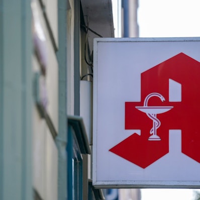 Ein Apotheken-Logo hängt an der Eingangsfassade einer Apotheke.