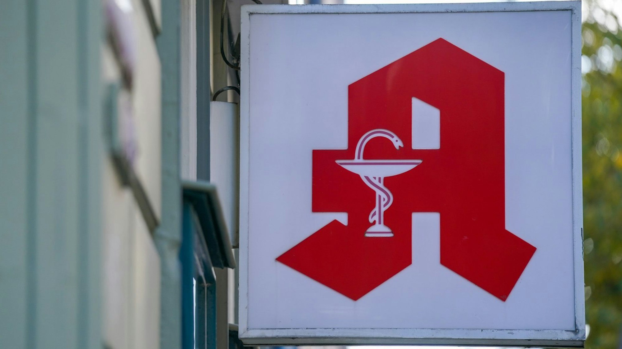Ein Apotheken-Logo hängt an der Eingangsfassade einer Apotheke.